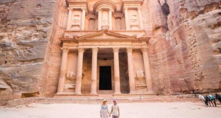 A couple stands before the grand sandstone façade of Petra’s Treasury in bright daylight.
