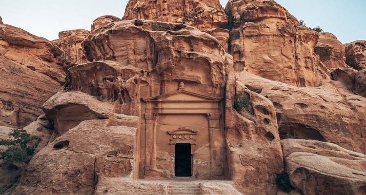 A small carved rock tomb is set into rugged sandstone walls in Petra.