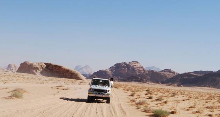 4x4 jeep drives along sandy track between rocky outcrops in Wadi Rum desert on a clear day