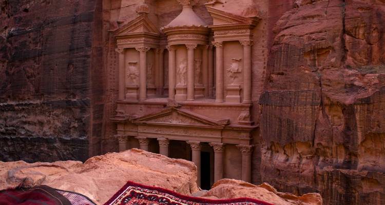 Petra Treasury viewed from a high ledge with patterned Bedouin rug in foreground in soft evening light