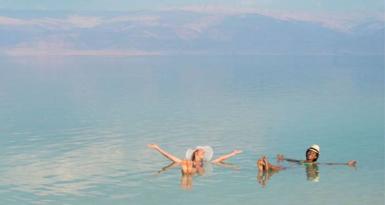 Two people float effortlessly in calm turquoise water with distant hazy mountains behind.