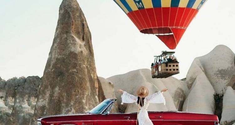 Mujer parada sobre un coche con un globo aerostático arriba.