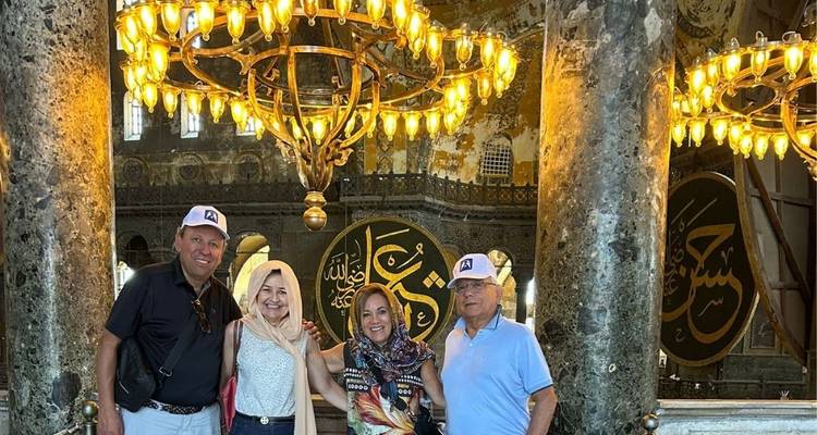 Grupo posando bajo una lámpara de araña en un interior histórico.