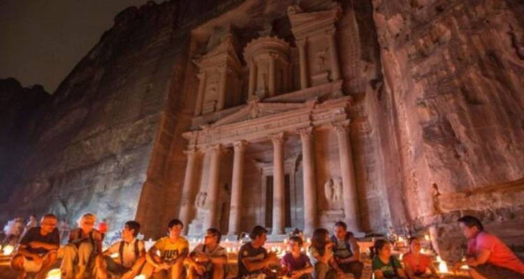 Travelers sit by candlelight in front of Petra’s Treasury carved into towering rock walls during an evening experience.