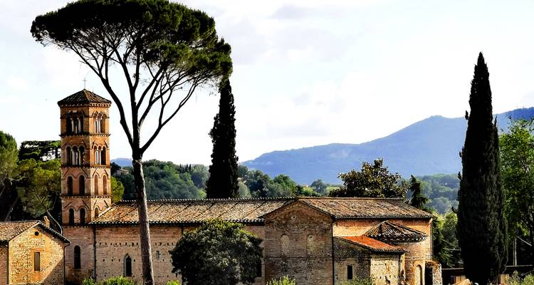 Bâtiment historique avec un grand arbre et un arrière-plan montagneux.