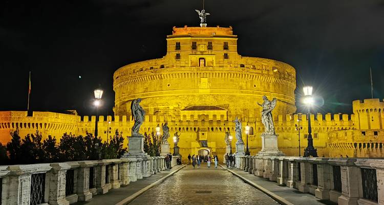 Vue nocturne d'un grand château avec des statues et des lumières.