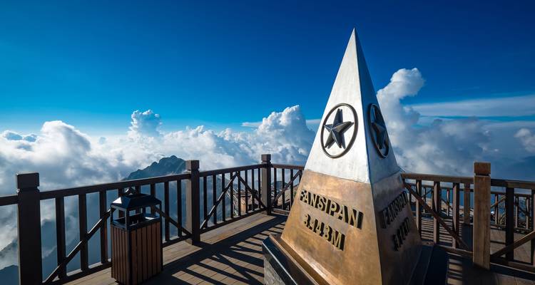Nahaufnahme eines hohen Denkmals in großer Höhe mit Blick auf Wolken und Berge.
