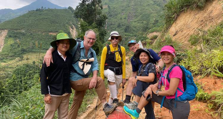 Gruppe von Menschen, die auf einem Hügelhang sitzen, mit terrassierten Feldern im Hintergrund.