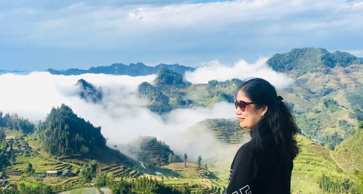 Frau genießt den malerischen Blick auf ein Tal mit Wolken über terrassierten Feldern.