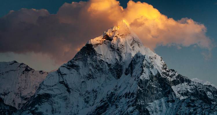 Besneeuwde bergtop bij zonsondergang met gouden wolken.