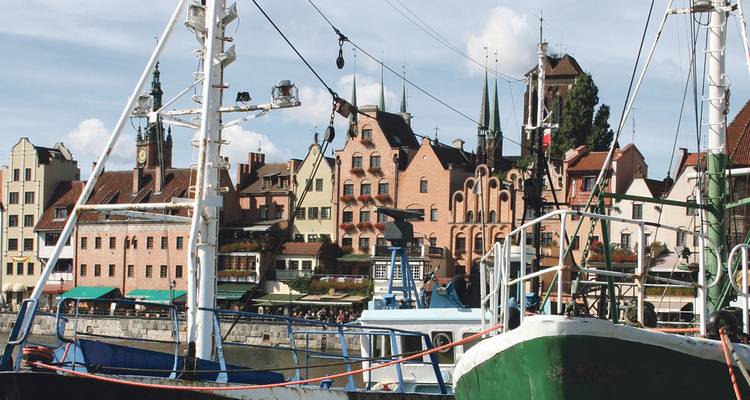 Blick auf Fischerboote und historische Gebäude an der Uferpromenade einer Stadt.