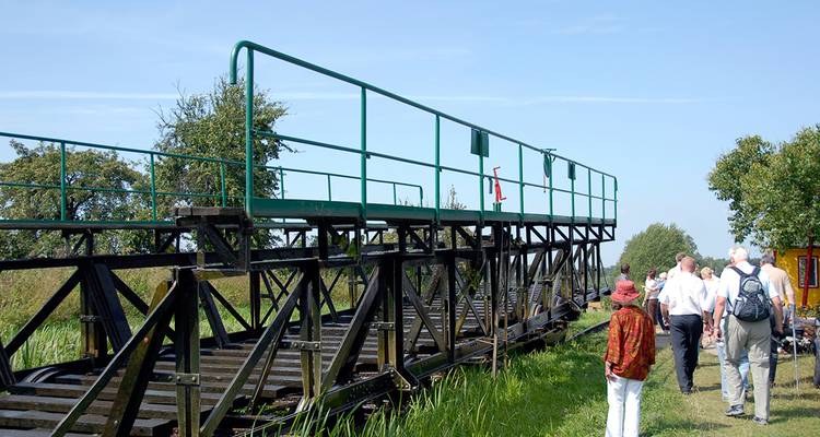Gruppe von Touristen, die in der Nähe eines Grasfeldes und einer mechanischen Struktur spazieren gehen.