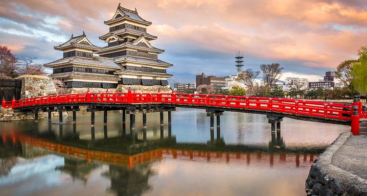 Traditionelle japanische Burg mit einer roten Brücke über einem Burggraben bei Sonnenuntergang.