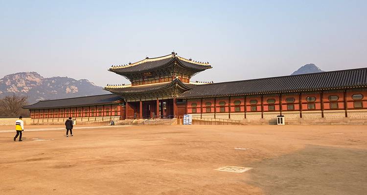 Vaste cour devant le palais Gyeongbokgung de Séoul avec quelques visiteurs et un arrière-plan montagneux.