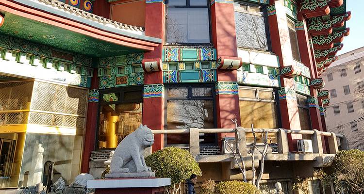 Façade décorative d'un bâtiment coréen ornée de motifs traditionnels colorés et d'un gardien de pierre.