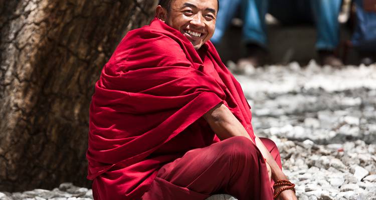 Mönch in roter Robe sitzend und lächelnd.