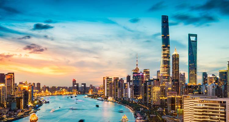 Skyline van een moderne stad bij zonsondergang met een rivier die erdoorheen stroomt.