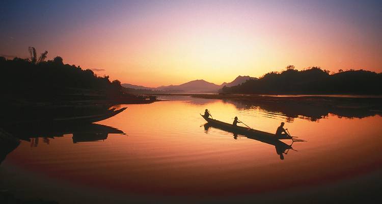 Drei Personen rudern ein Boot bei Sonnenuntergang.