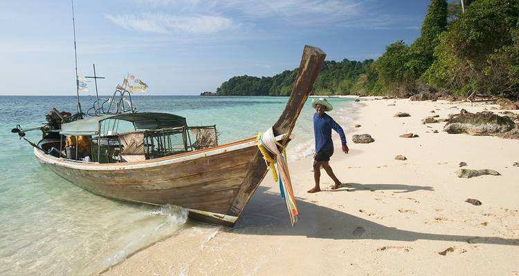 A longtail boat on a sandy beach with clear waters.