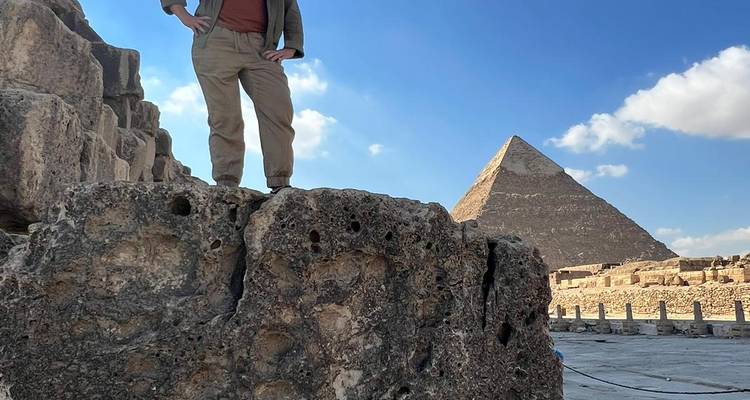 Persoon poseert met piramide op de achtergrond.