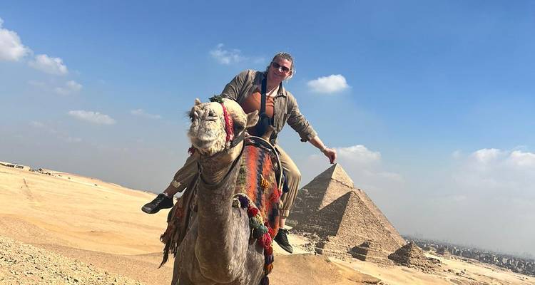 Persoon die op een kameel rijdt met piramides in zicht.