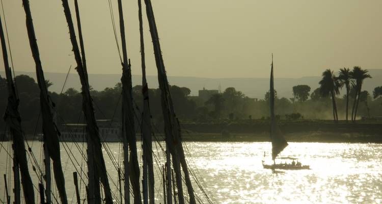 Silhouet van een zeilboot op een rivier tijdens zonsondergang.