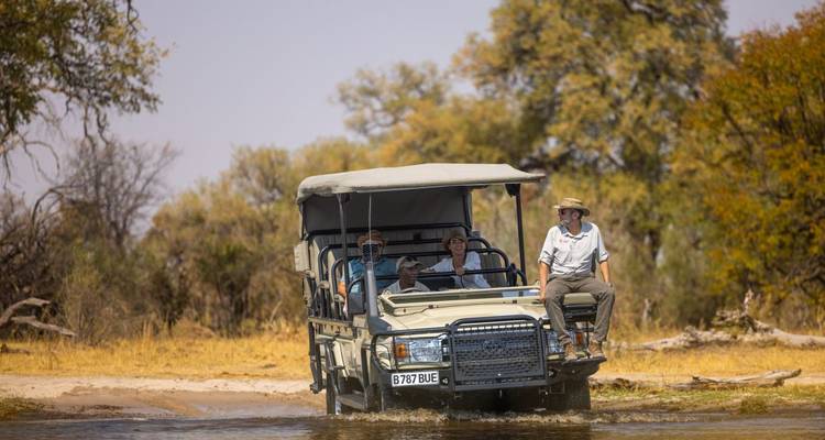 Safarifahrzeug überquert Wasser mit Passagieren.