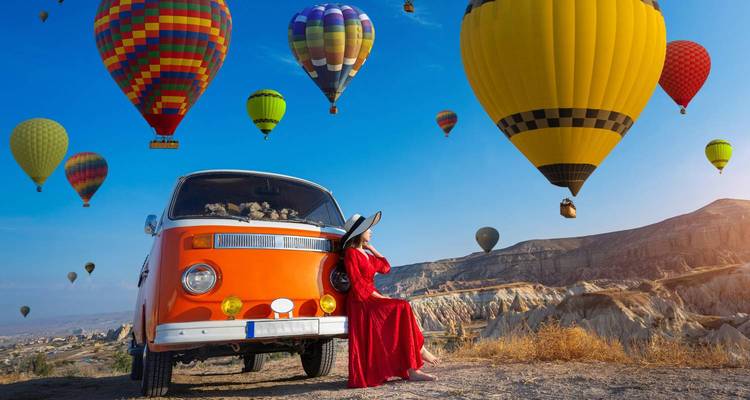 Persona sentada en una camioneta con globos aerostáticos en el cielo.