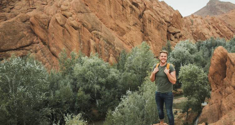 Homme posant devant un paysage rocheux avec des arbres.
