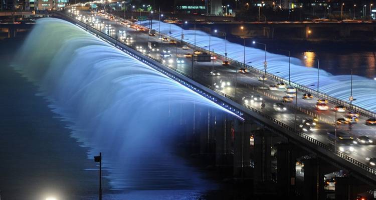 Bridge with illuminated water feature at night.