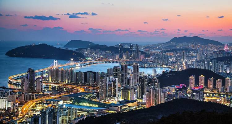 Panoramic view of a coastal city with illuminated bridges at dusk.