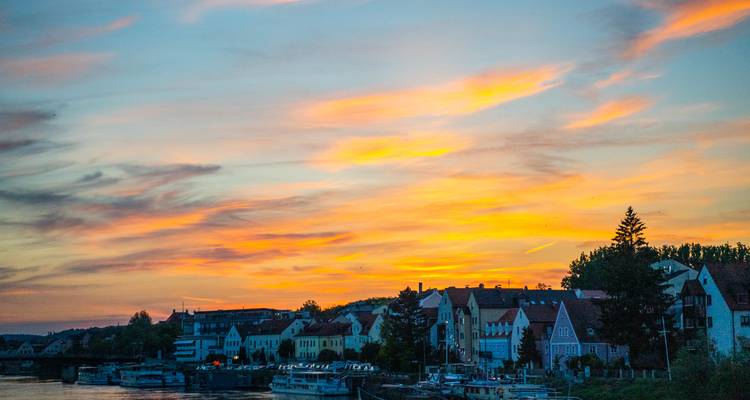A sunset view of a riverside town with vibrant skies and silhouetted buildings.