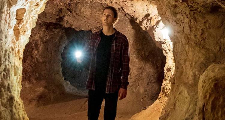 A traveler holding a flashlight explores narrow sandstone tunnels in an underground cave dwelling.
