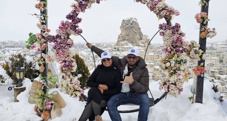 Una pareja sentada en un columpio floral con paisajes cubiertos de nieve detrás.