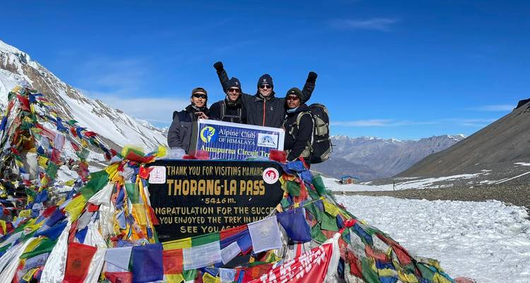 Gruppenfoto vor Beschilderung mit bunten Fahnen und verschneiten Bergen.