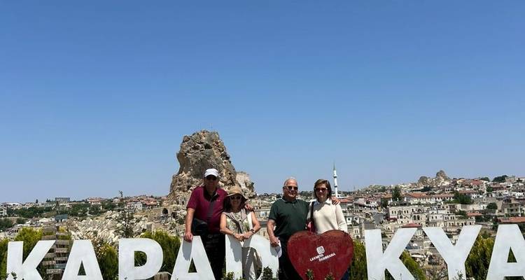 Grupo de personas posando junto a un letrero de 'Kapadokya' con formaciones rocosas.