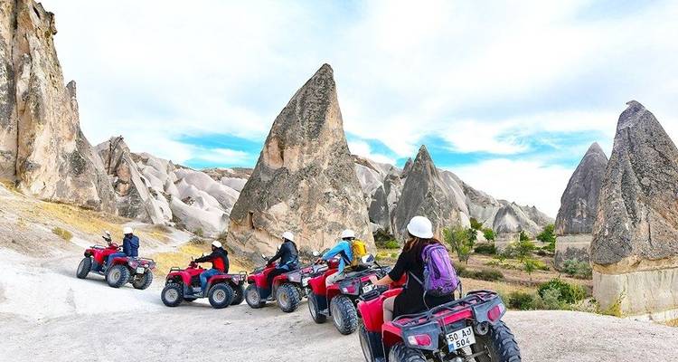 Conductores de cuatrimotos en un sendero entre formaciones rocosas.
