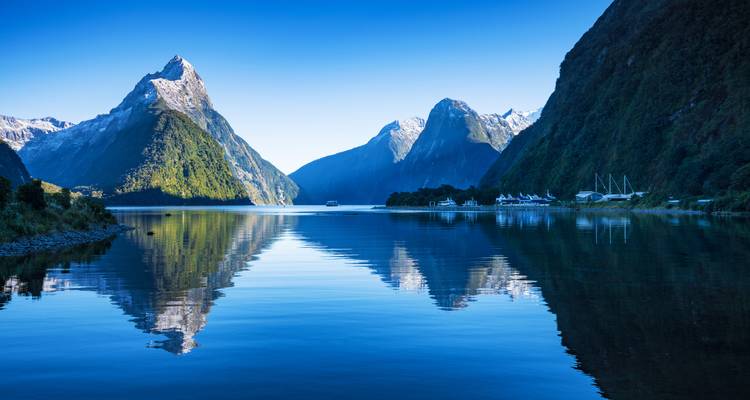 Les pics emblématiques de Milford Sound reflétés parfaitement dans les eaux bleues calmes sous un ciel dégagé