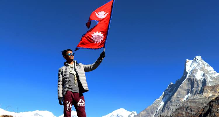 Persona sosteniendo banderas nepalesas con un fondo montañoso.