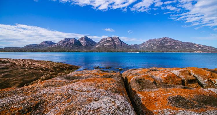 Bergen die een kalme blauwe zee ontmoeten met een rotsachtige voorgrond.