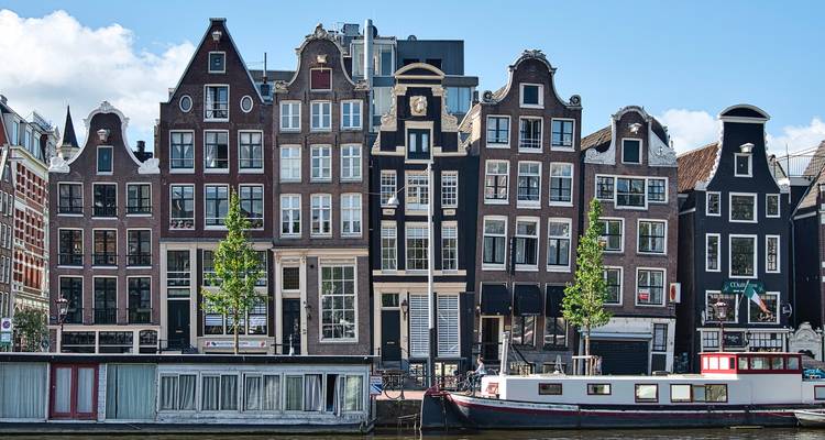 Rij met klassieke Nederlandse trapgevelgevels weerspiegeld in het kanaal onder een helder lucht.