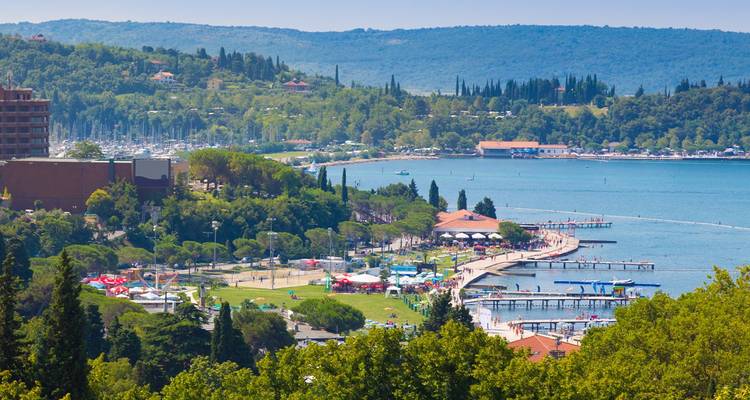 Luftaufnahme der Küste von Portoroz mit geschwungener Promenade, grünen Parks und vor Anker liegenden Booten