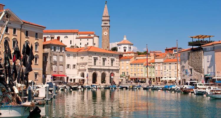 Der charmante Hafen von Piran mit bunten Booten und einem mittelalterlichen Glockenturm, der sich über pastellfarbenen Gebäuden erhebt