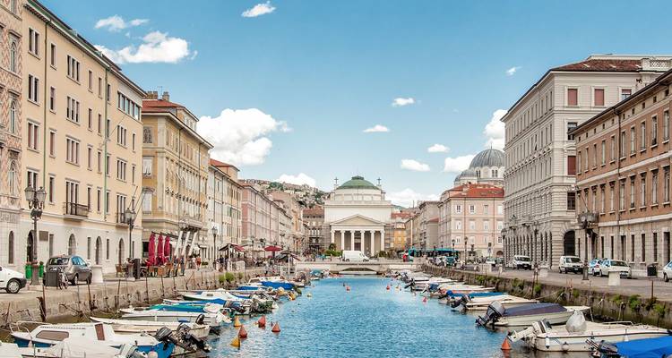 Der Große Kanal von Triest mit neoklassizistischen Gebäuden und kleinen vertäuten Booten unter blauem Himmel