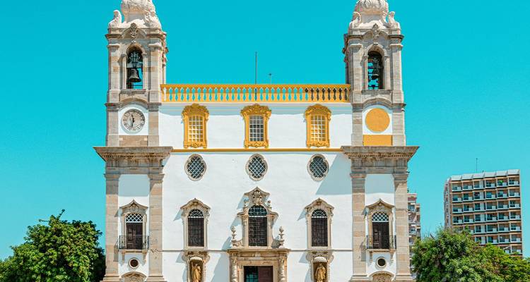 Fachada blanca de estilo Barroco de la Iglesia del Carmo de Faro con sus dos campanarios gemelos bajo un cielo turquesa vibrante