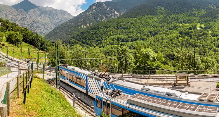 Tren de rayas azules serpenteando a través de un exuberante valle montañoso verde bajo un cielo soleado
