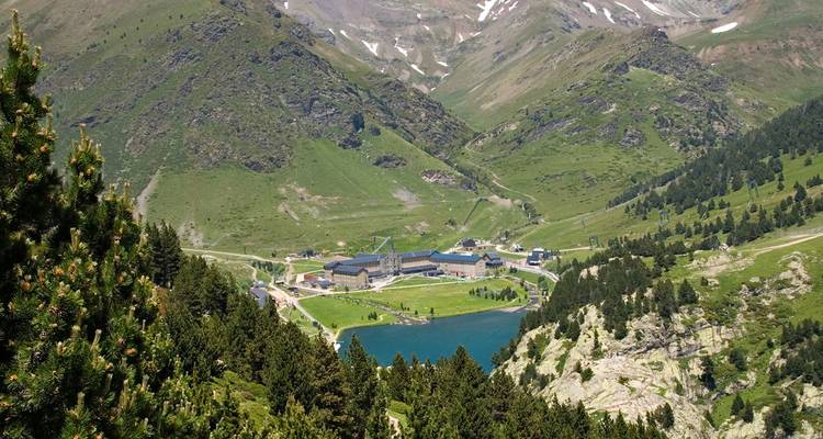 Valle alpino exuberante con un lago turquesa y un complejo de montaña rodeado de bosques de pinos en los Pirineos