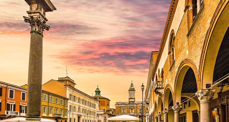 Une place pittoresque avec une architecture historique sous un ciel de coucher de soleil coloré.
