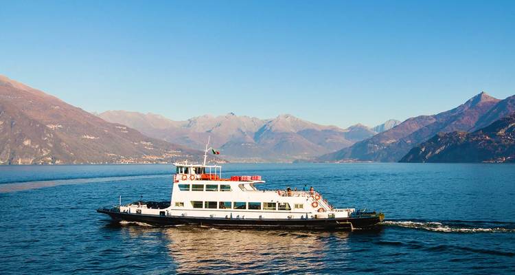 Passenger ferry sailing across the calm blue waters of Lake Como surrounded by mountains.