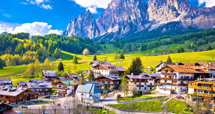 Pueblito alpino acurrucado bajo los picos dentados de las Dolomitas bajo un cielo brillante.